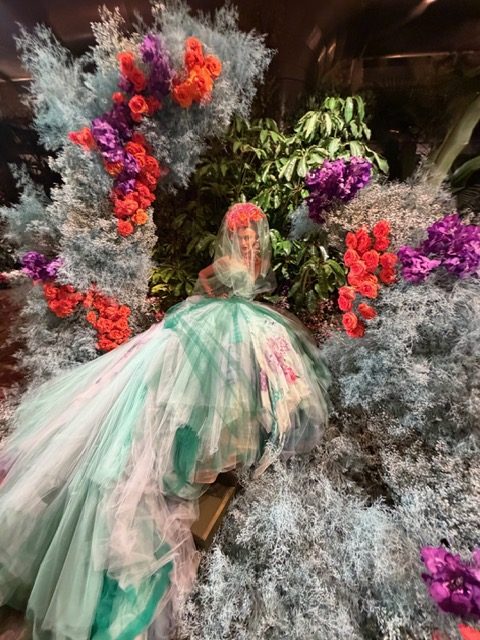 A voluminous mint and blush tulle gown staged among blue foliage and bright blooms